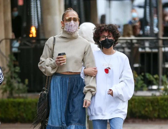 Jennifer Lopez in a tan sweater and blue skirt walking with her child Emme