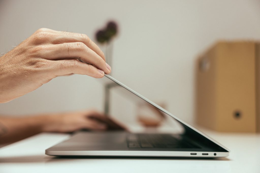A hand lowers the lid of a laptop computer on a desk