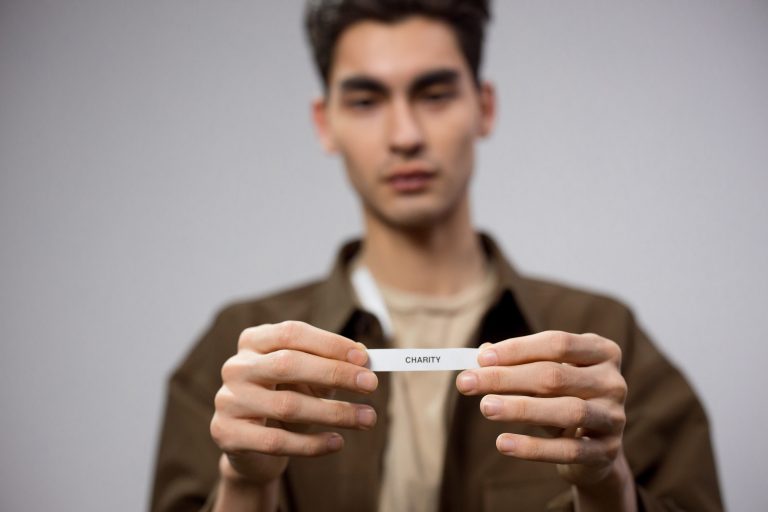 A man holds a note reading 'charity,' with the focus on his hands, expressing a charitable theme