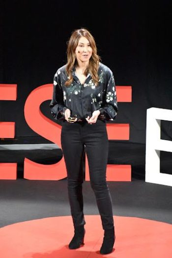 Leslie Saglio sdtanding on a stage at a Ted event giving a talk