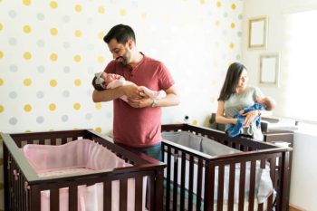 Latin loving parents carrying their twin babies by cribs at home